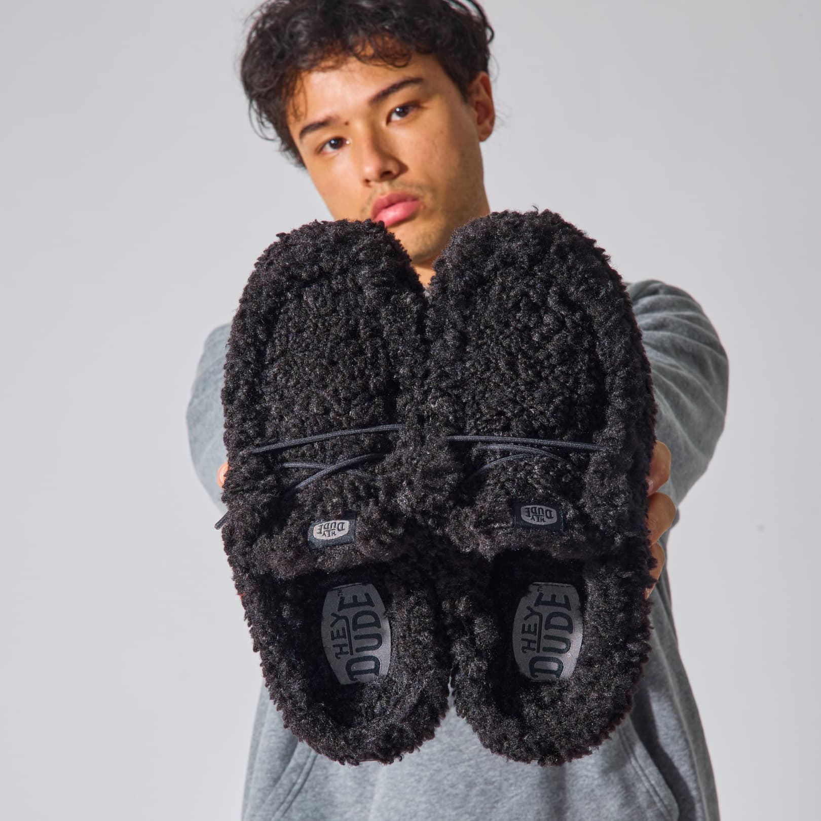 man holding a pair of the best hey dude slippers. Comfortable black slippers. Lightweight easy slip on shoes.